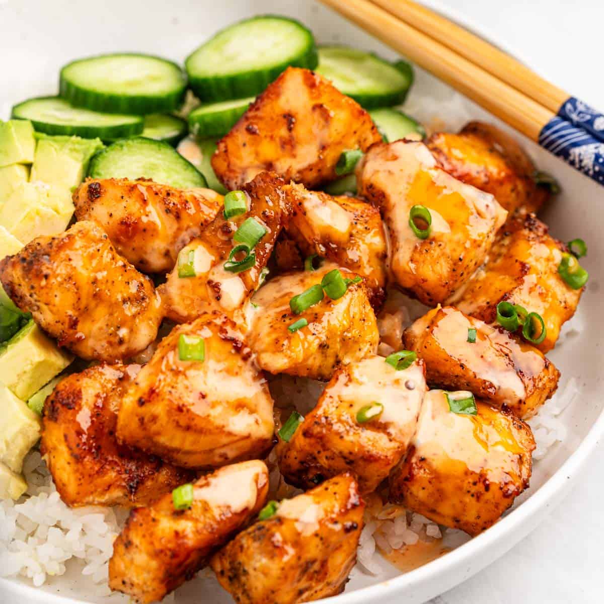 plate of air fryer salmon bites on bed of rice with slices of cucumbers and avocado.