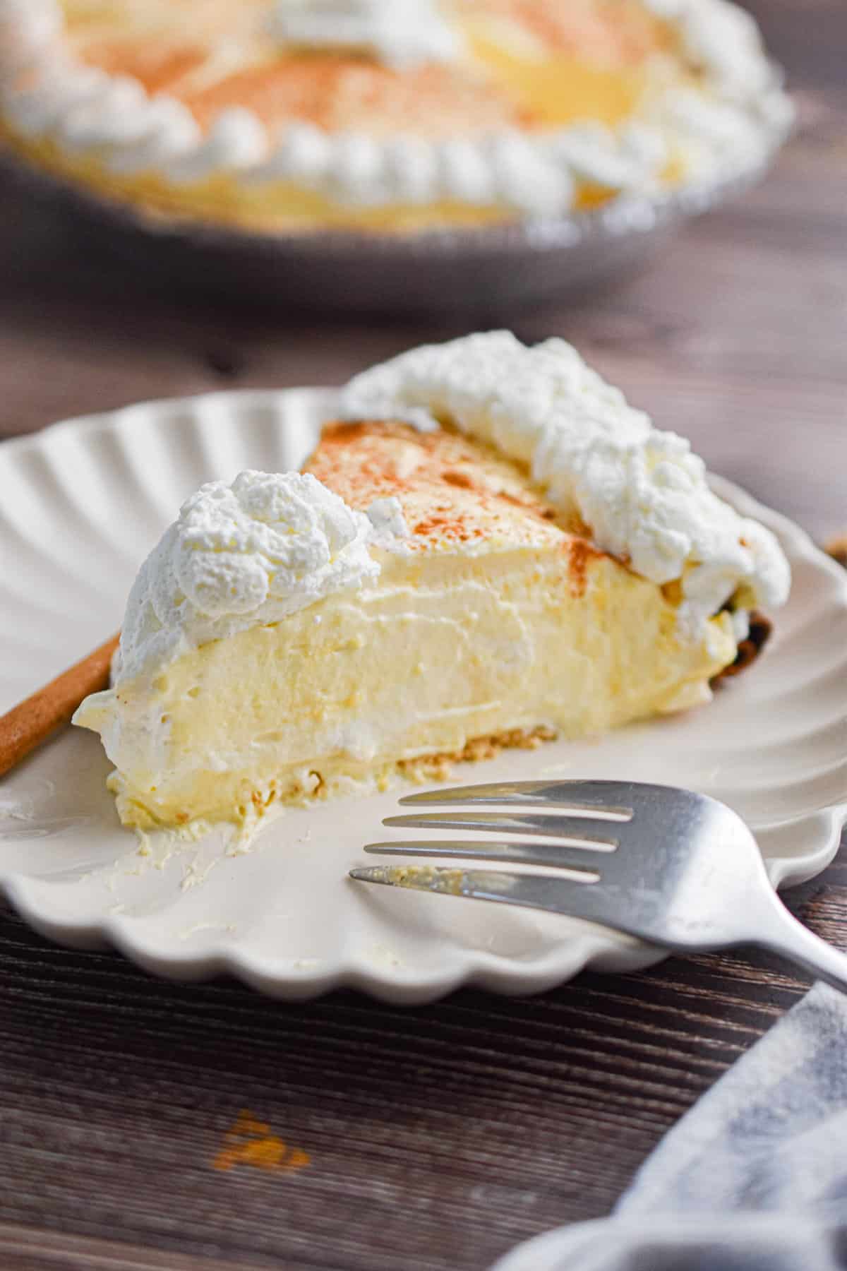 A slice of the no-bake eggnog pie is on a plate with a fork and a cinnamon stick.