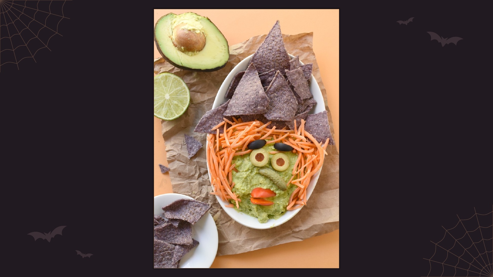 Guacamole arranged into a witch face with shredded carrot hair, olive eyes and blue corn tortilla chips