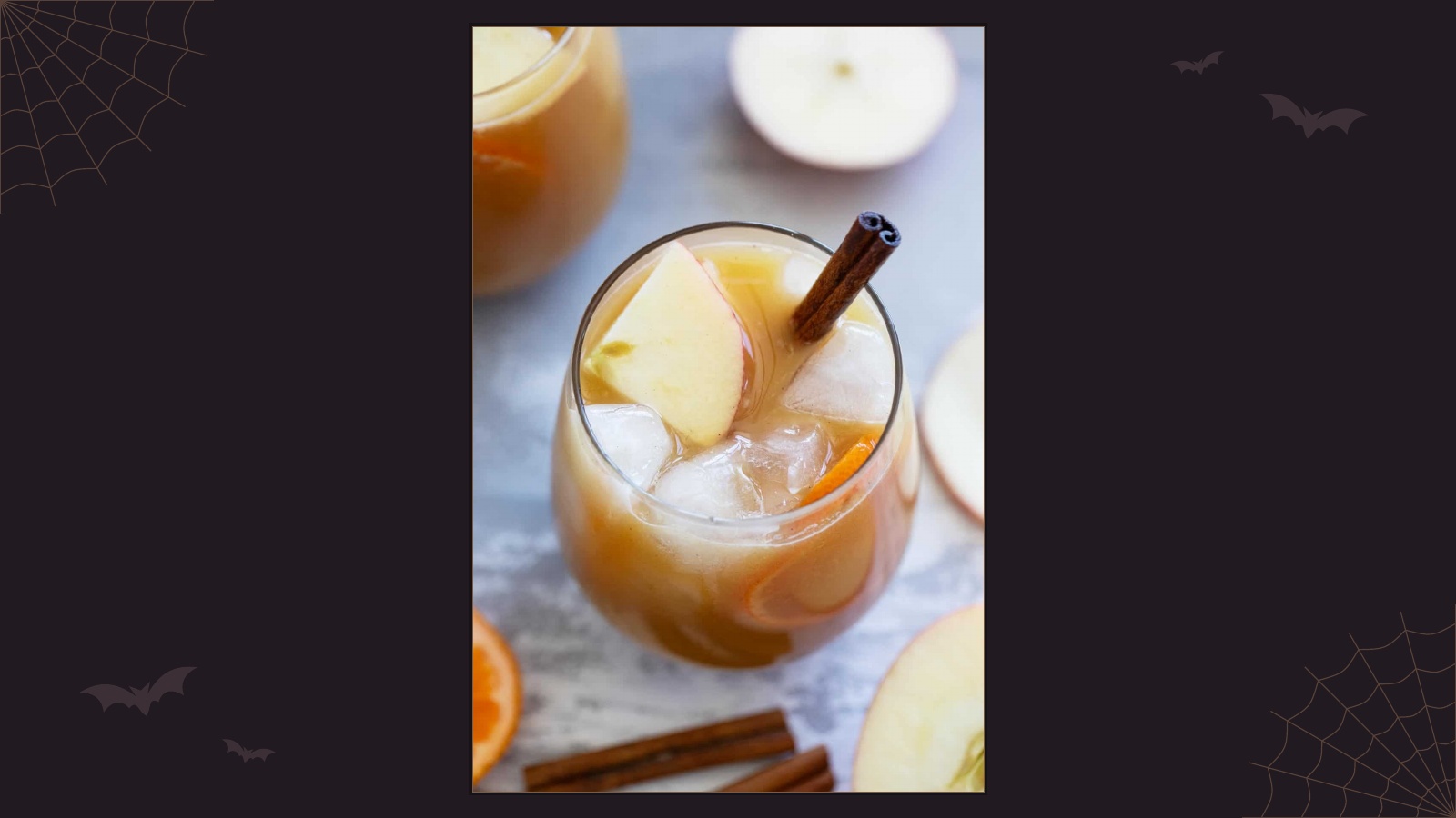 Glass of chilled spiced apple cider punch with sliced apples, orange and a cinnamon stick
