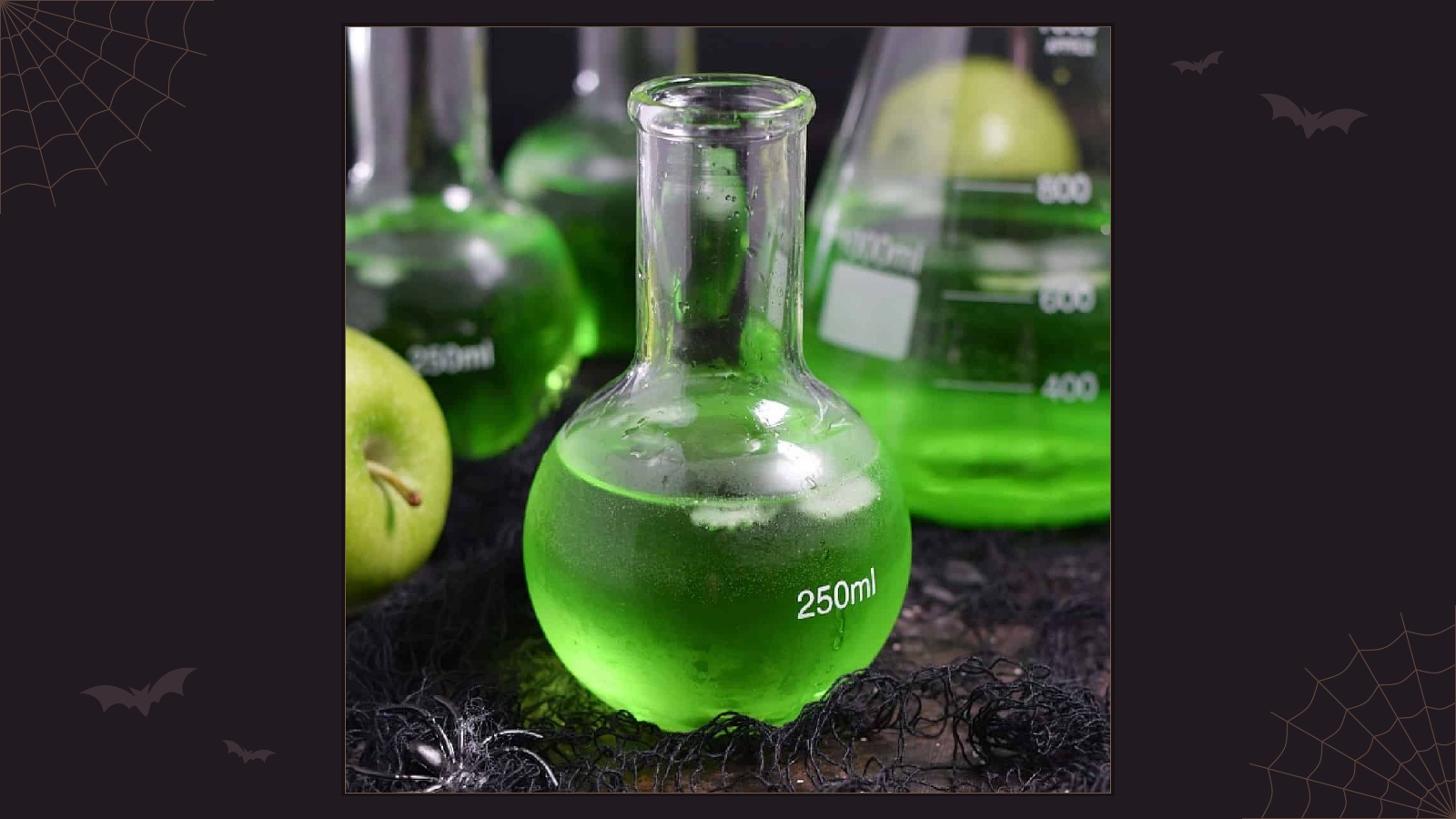 Bright green poisoned apple Halloween cocktail in glasses with apple slices and a science beaker