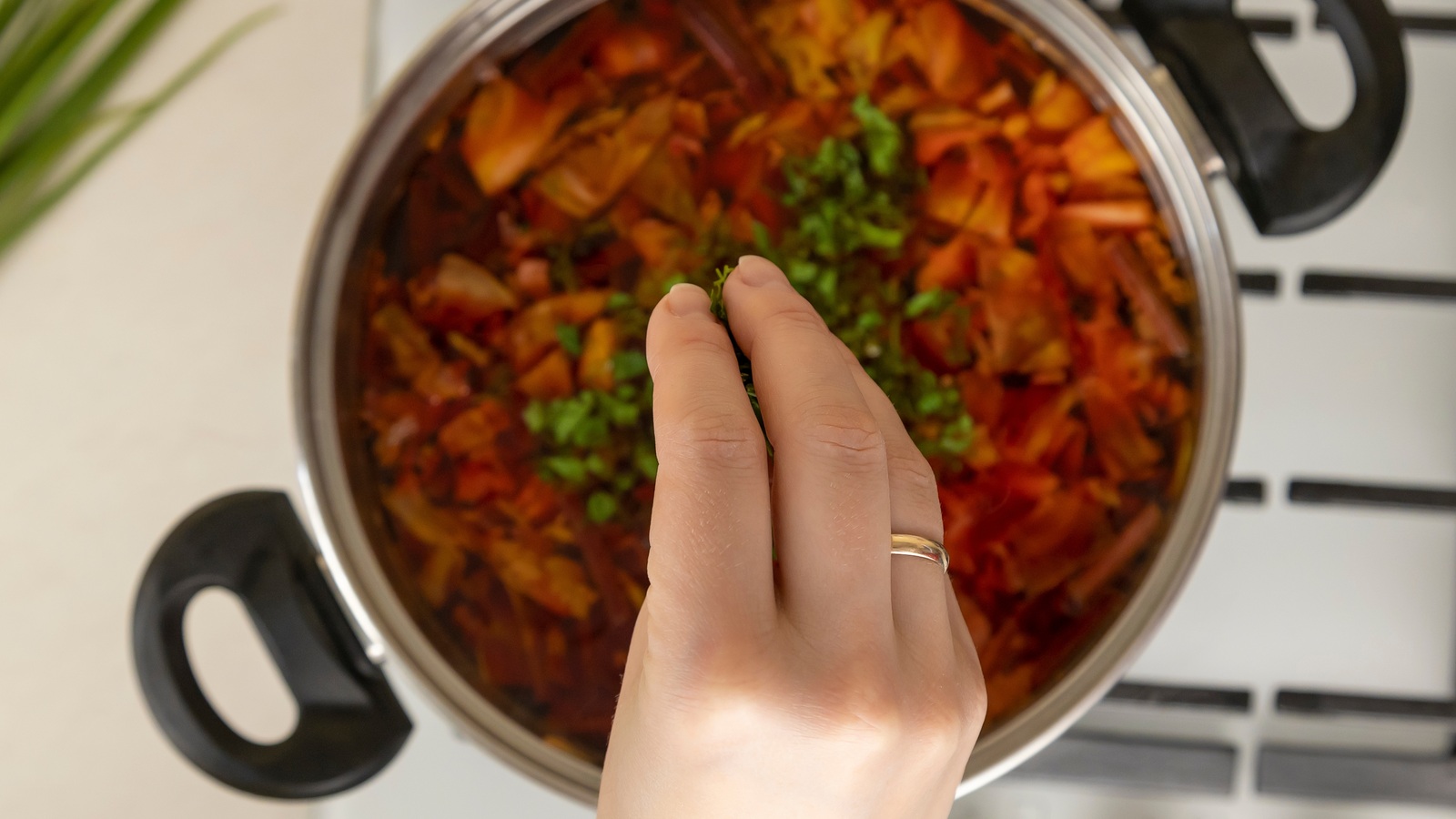 A hand sprinkling chopped green herbs into a pot of soup