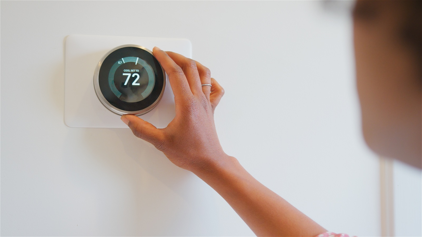 Woman adjusting a wall-mounted digital thermostat displaying 72 degrees