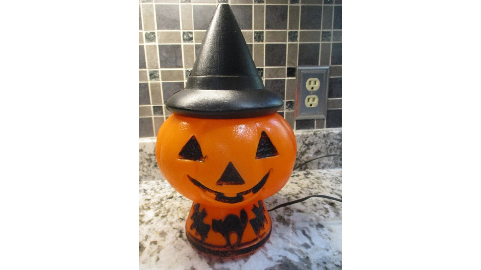 Orange Bayshore Pumpkin Witch with triangular eyes, smiling face, tall black witch’s hat and cat-and-bat decorated base.