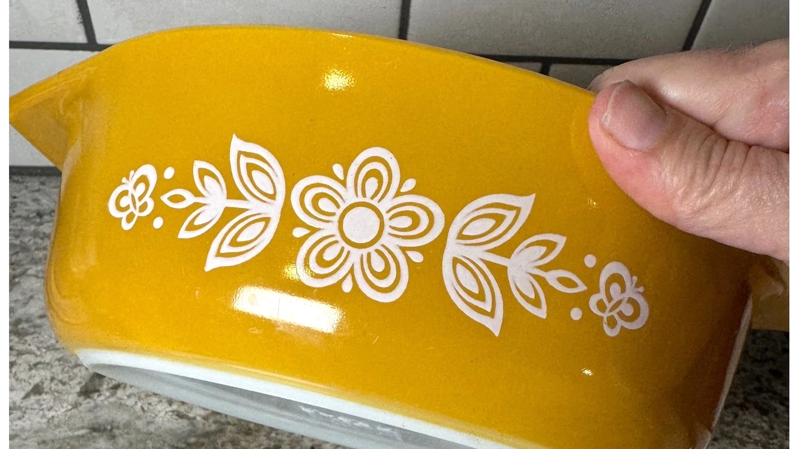Hand holding a gold Pyrex casserole to show its glossy finish and white floral pattern