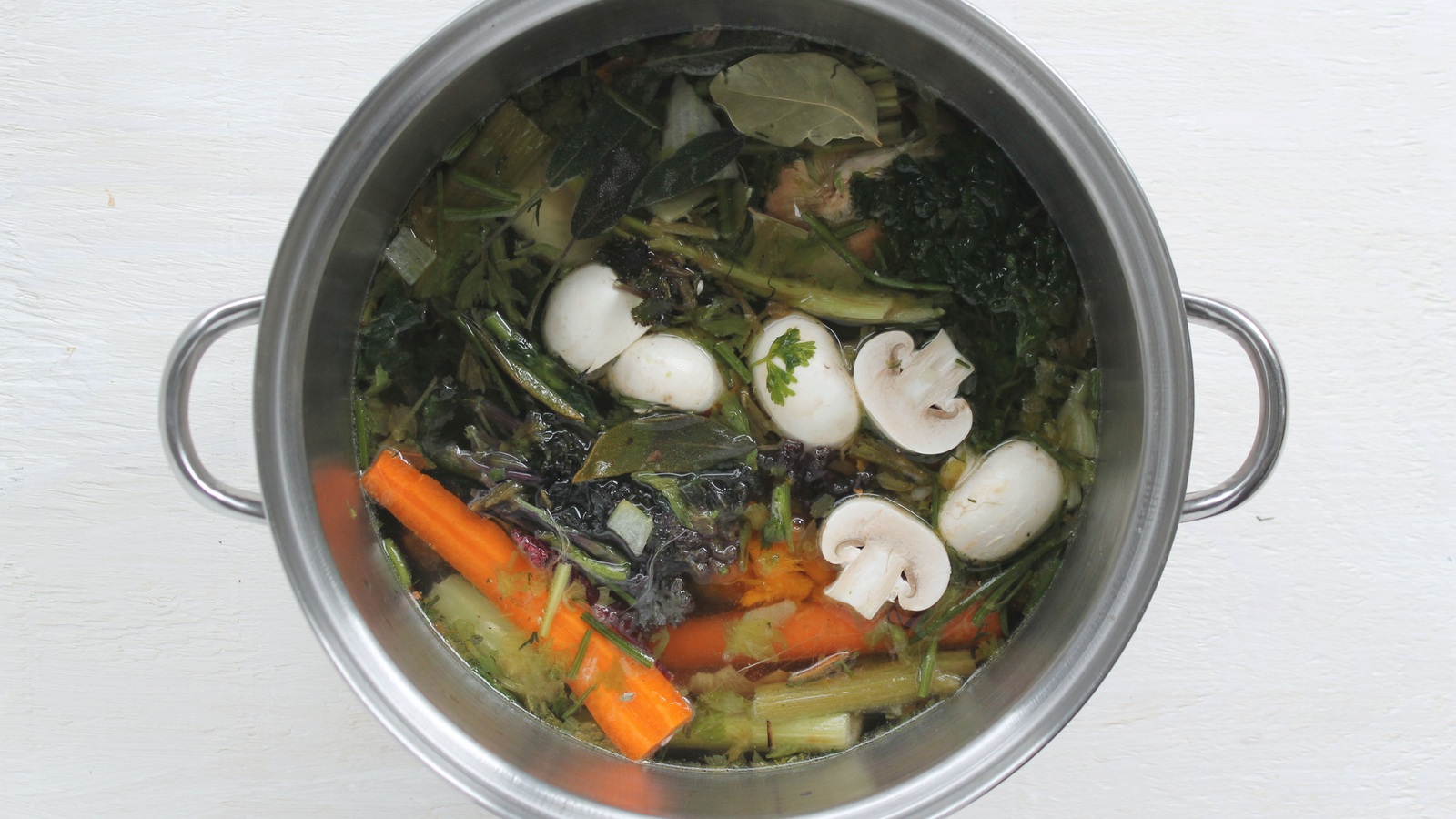 Celery stalk pieces, carrot trimmings, mushrooms, and leafy greens simmering in a stockpot