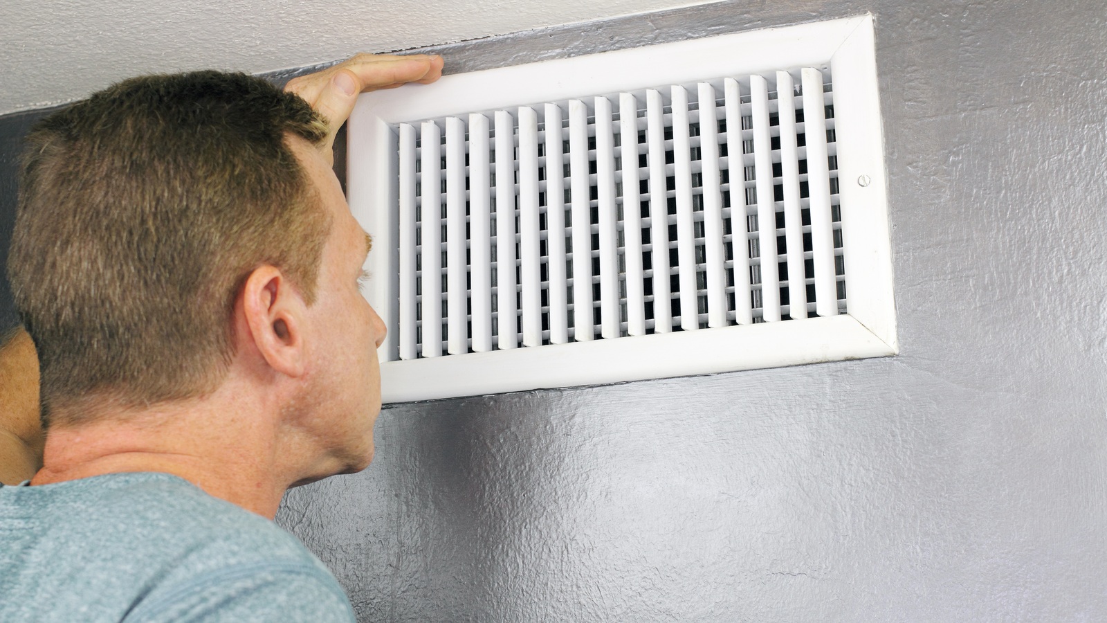 Man examining a white wall-mounted home air grille