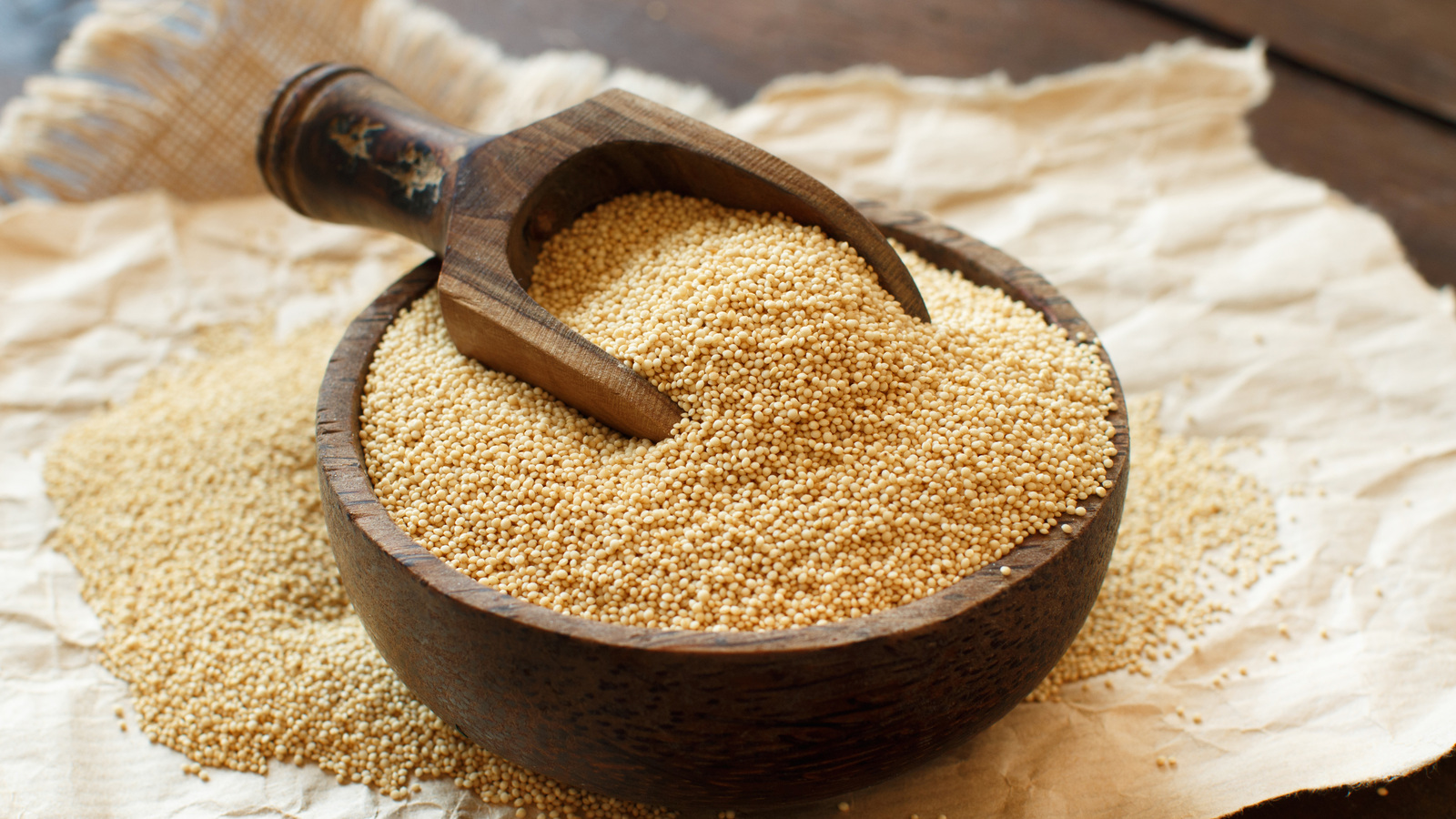 Tiny pale amaranth seeds in a wooden bowl with a scoop