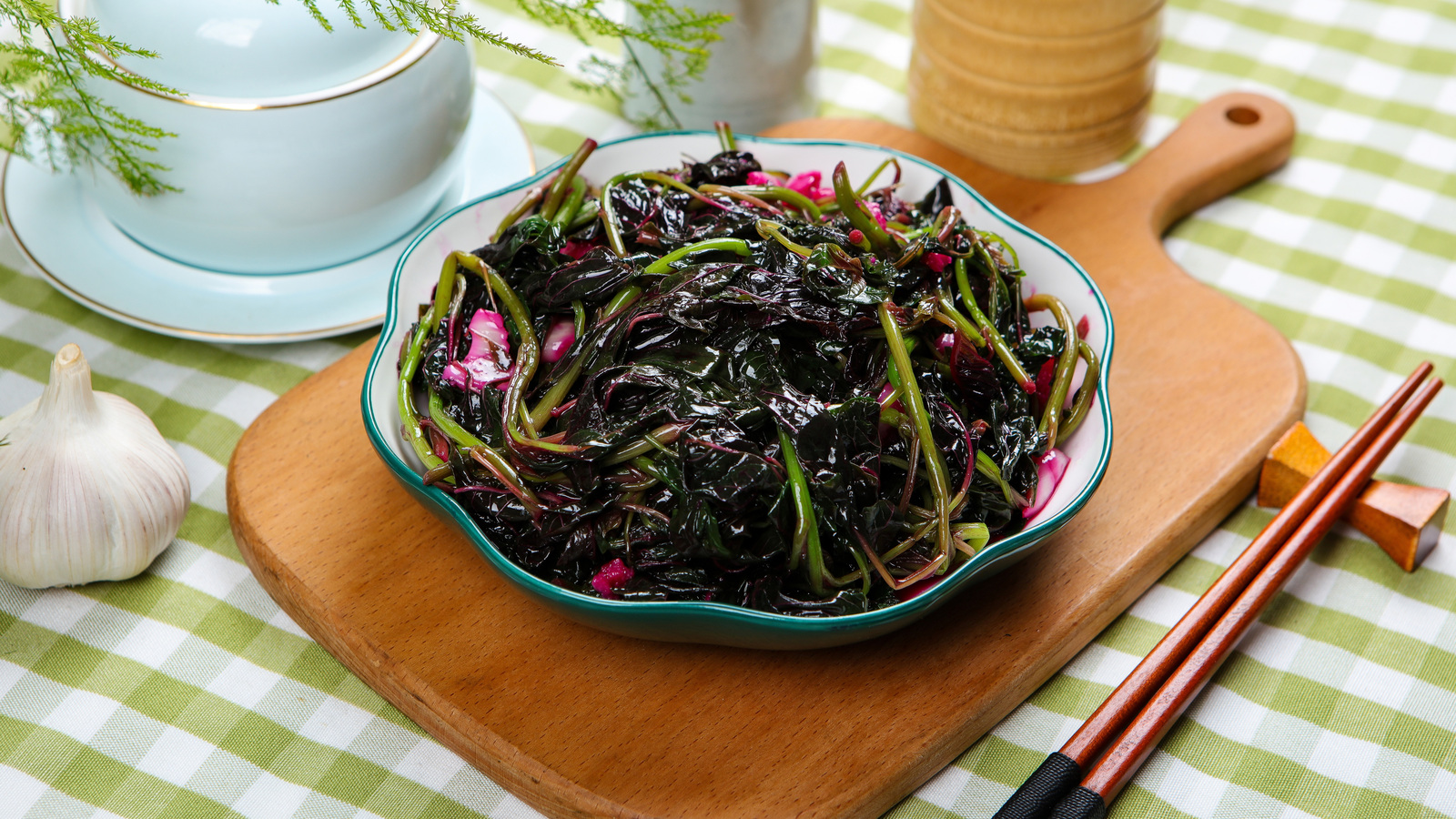 Bowl of cooked amaranth greens with garlic on a wooden board beside chopsticks