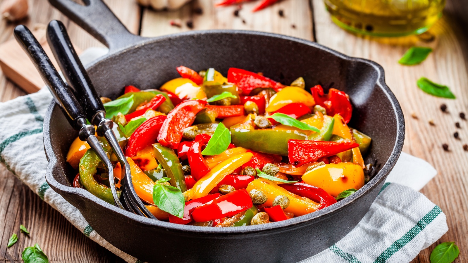 Red, yellow and green cooked peppers with basil and capers in a black skillet