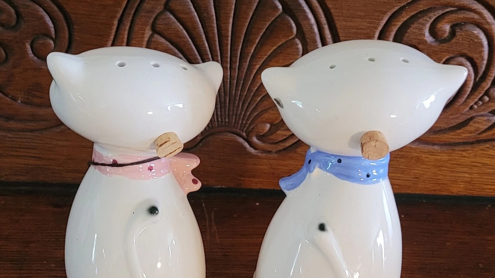 Backs of two Cozy Kittens shakers showing cork stoppers behind their heads and painted pink and blue scarves.