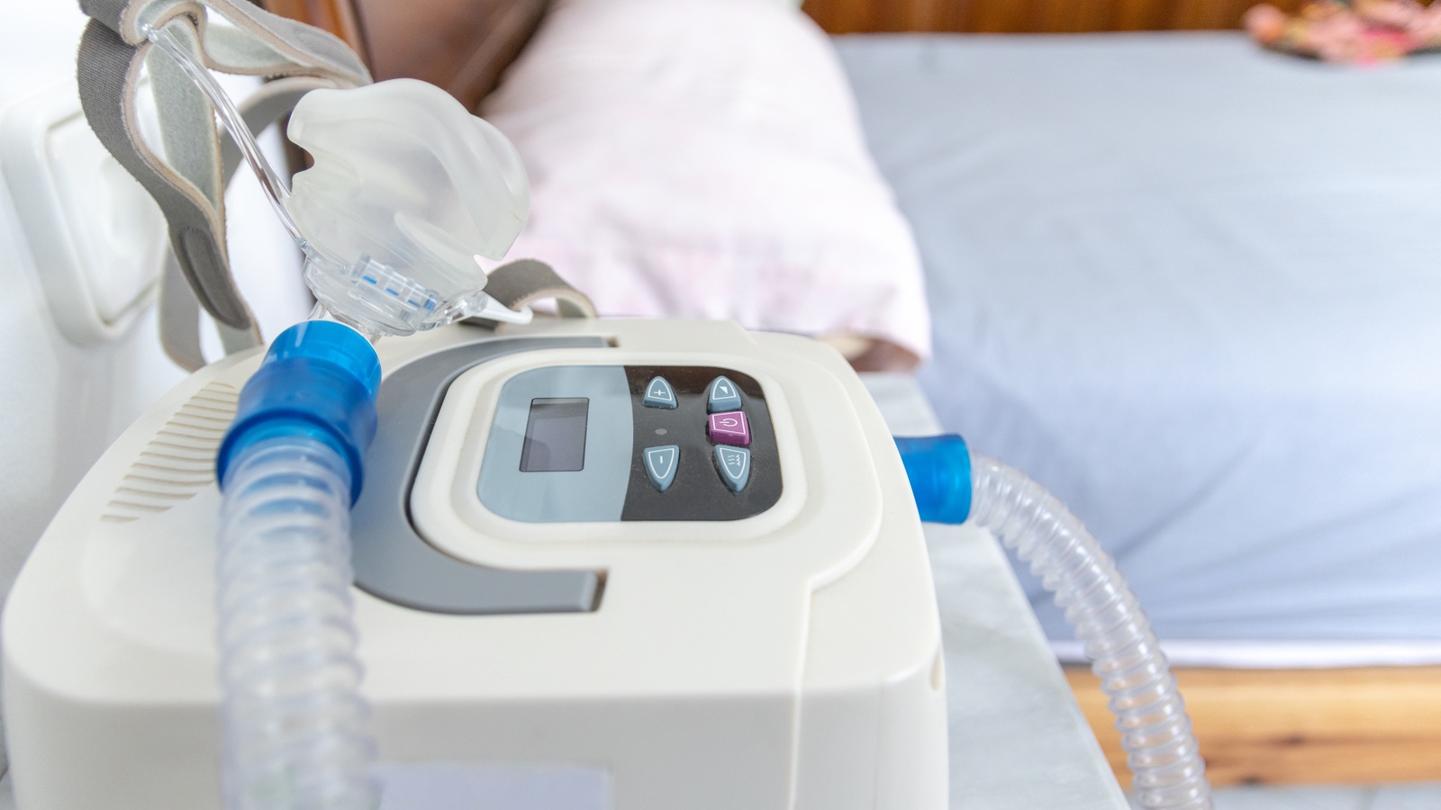 CPAP machine controls, hose and mask beside a bed