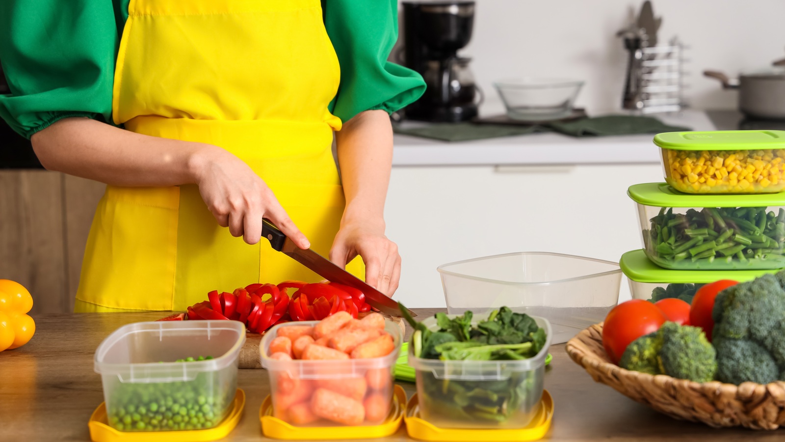 Woman cutting red bell pepper on a board beside vegetables and storage containers