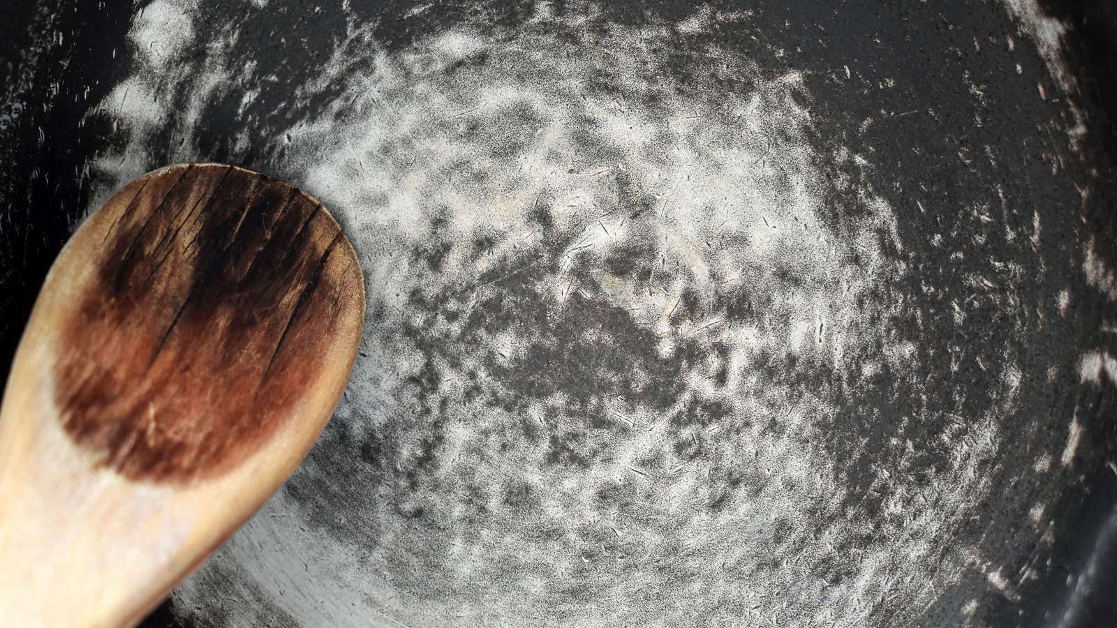 A badly scratched nonstick pan beside a wooden spoon