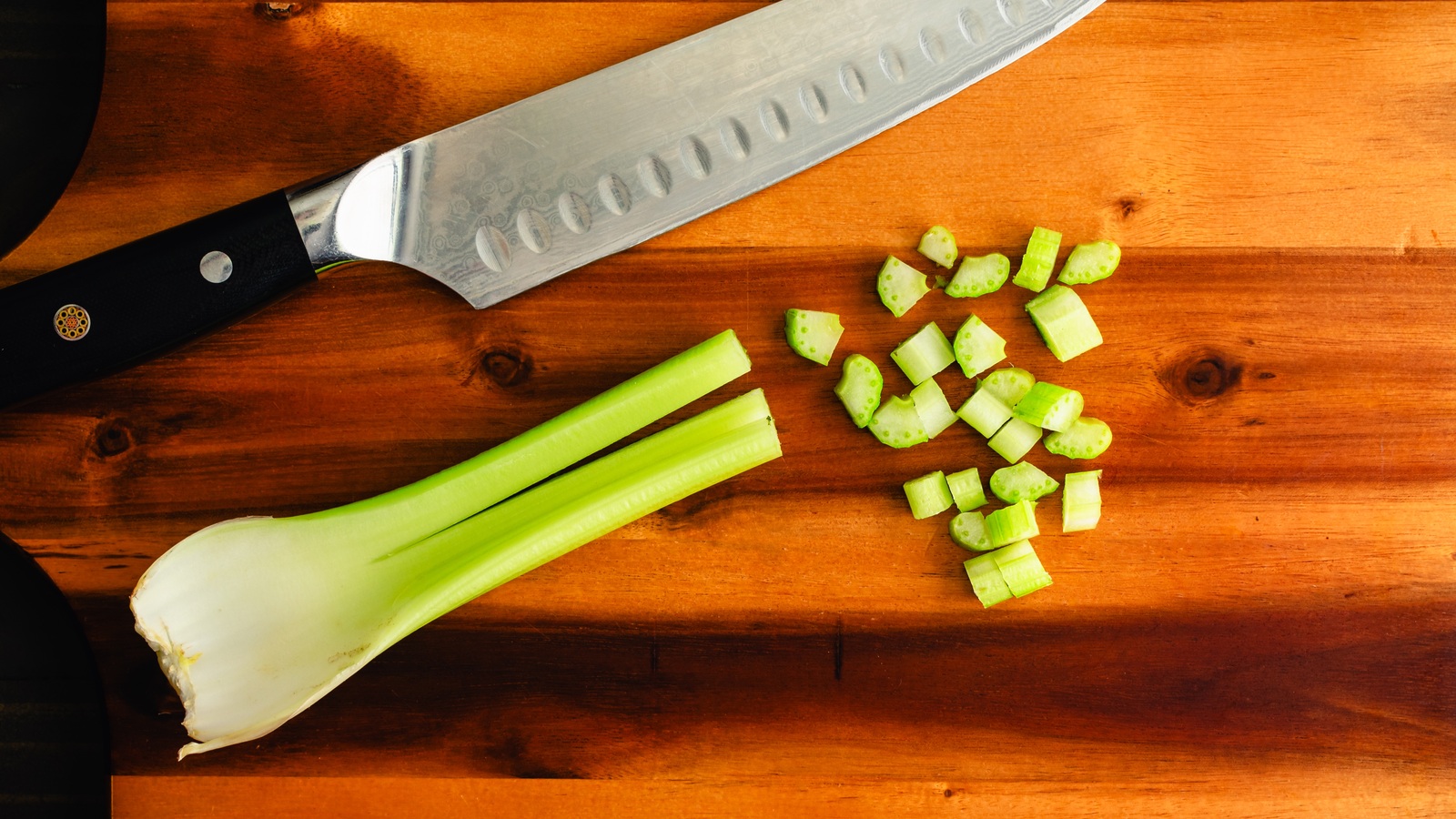 Diced celery and a short celery stalk beside a chef’s knife on a wooden cutting board