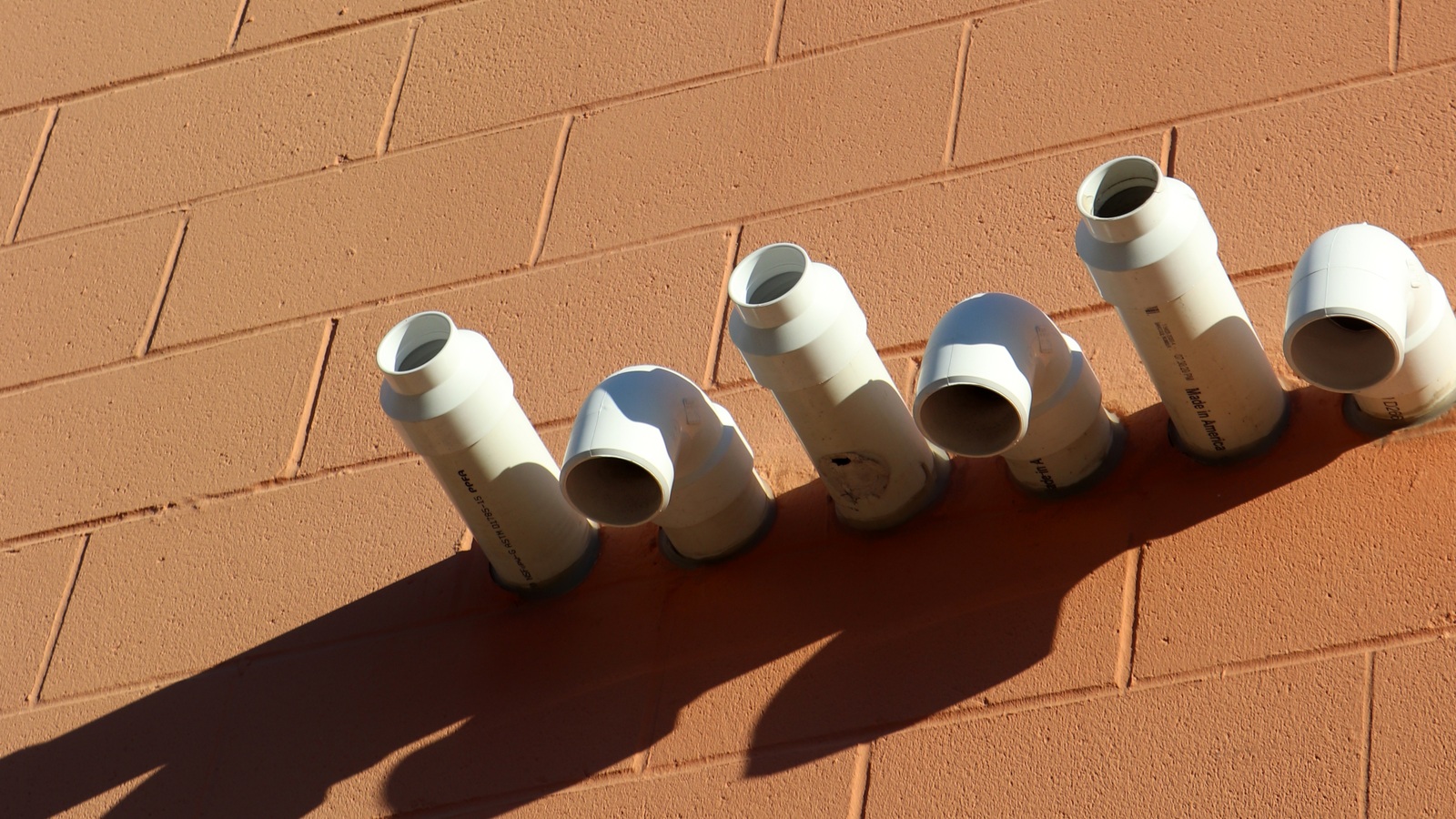 White furnace intake and exhaust pipes projecting from an exterior brick wall
