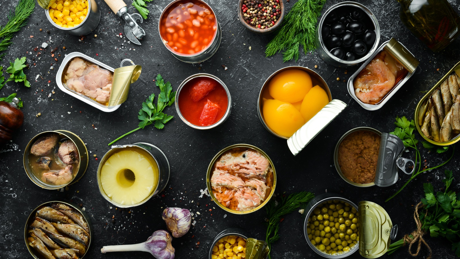 Open tins of vegetables, beans, fruit and fish arranged on a dark table