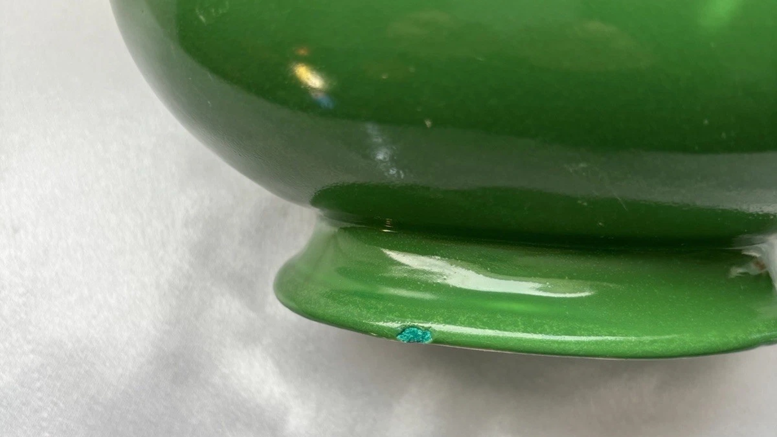 Close-up of a green Fiesta gravy boat foot showing a small nick with a blue-green touch-up.
