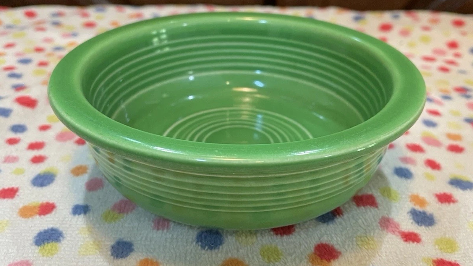Small vintage Medium Green Fiesta fruit bowl with concentric rings, photographed on a multicolored cloth.