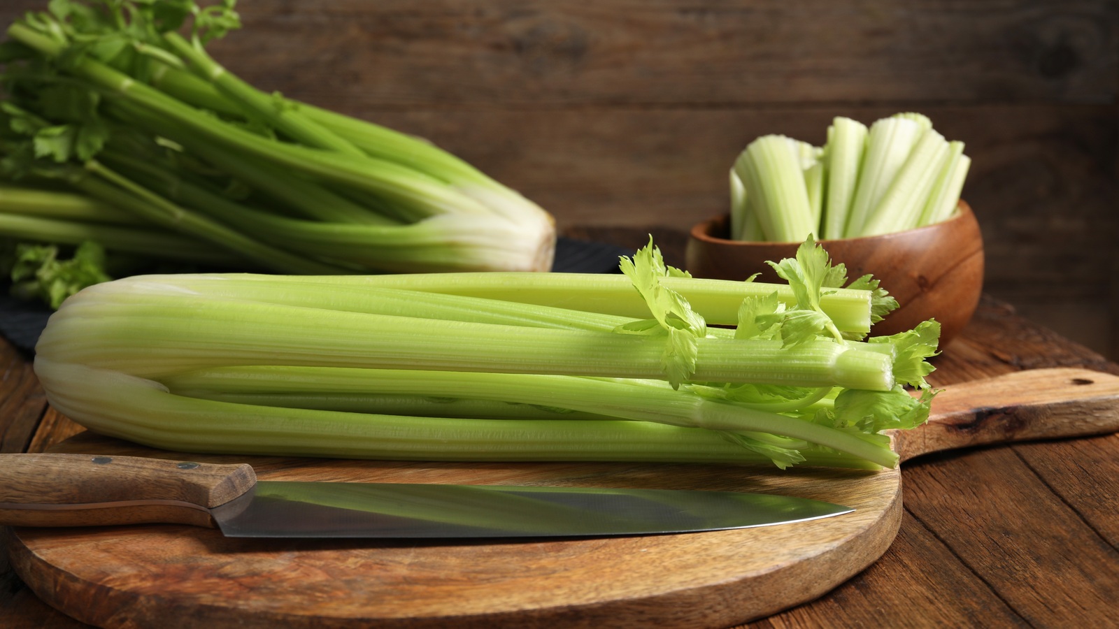 Fresh green celery bunches and cut stalks beside a knife on a wooden board