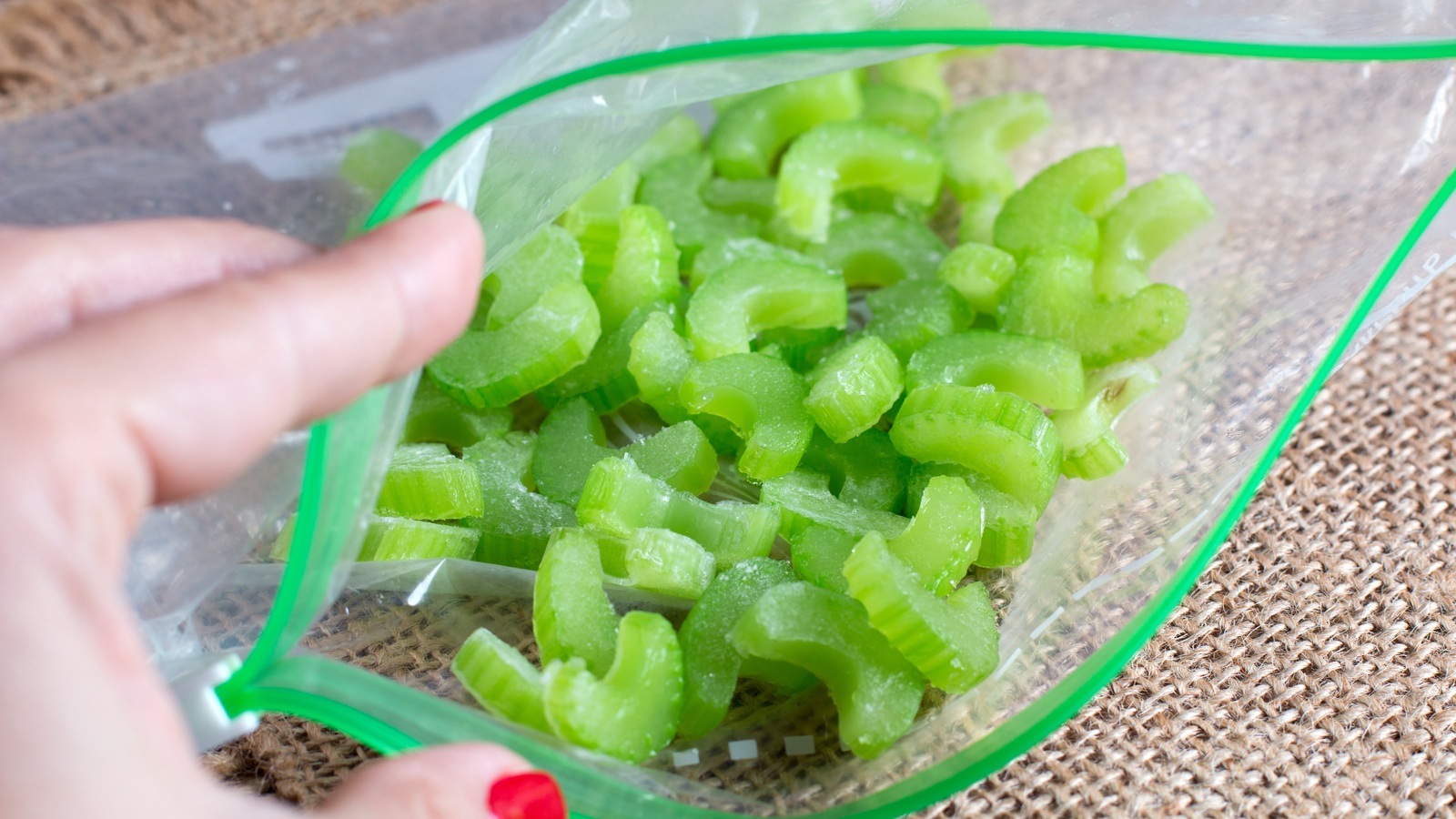 Chopped frozen celery pieces in a resealable freezer bag held open on a wooden surface