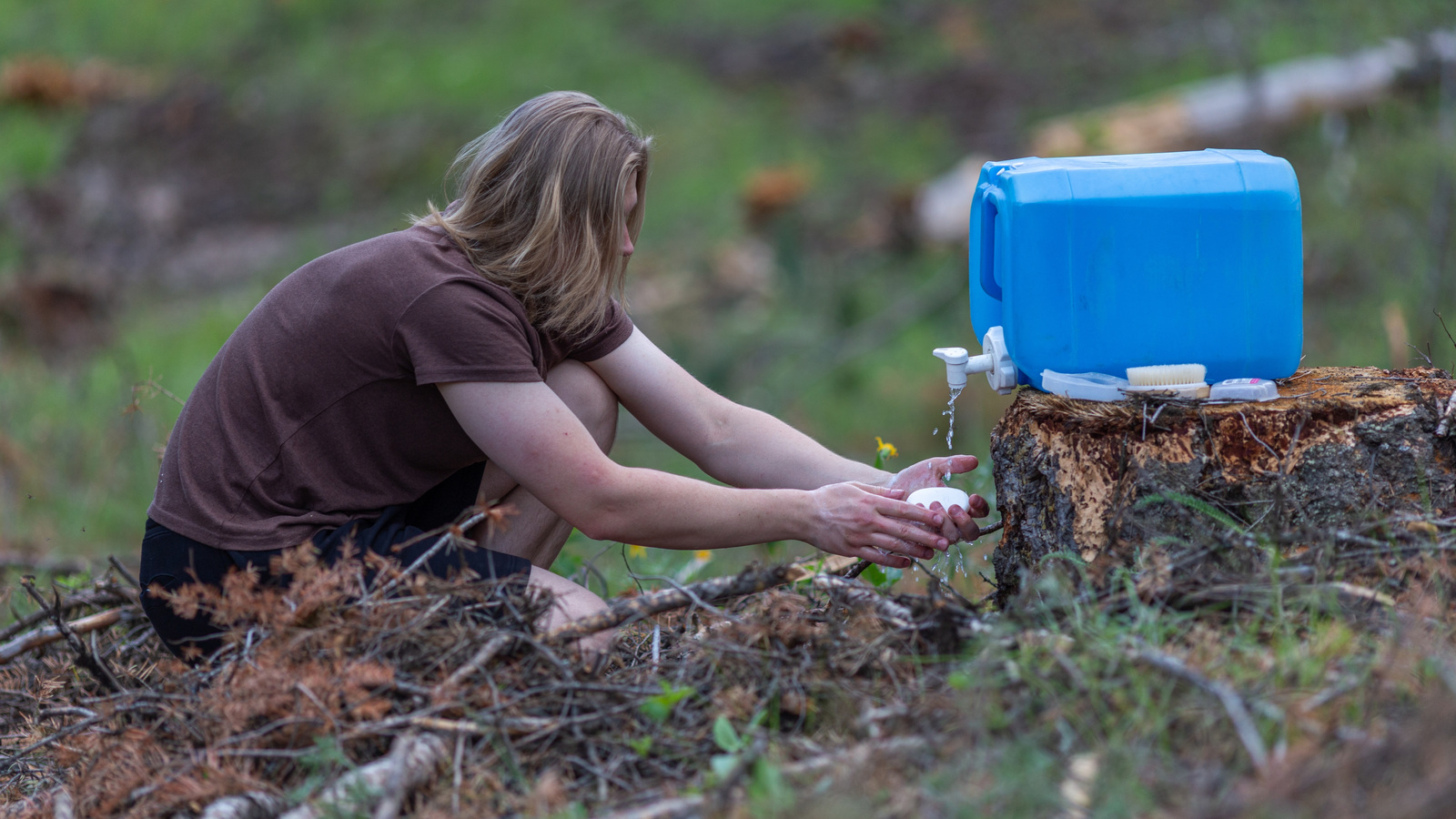 Person washing soapy hands under a tap on a blue water container outdoors