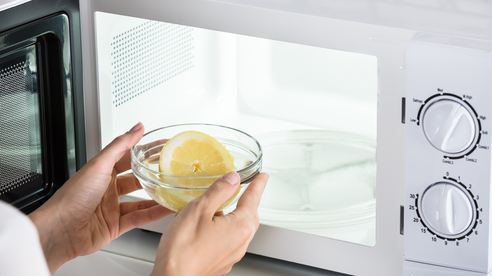 A woman placing a bowl of lemon slices and water in a microwave