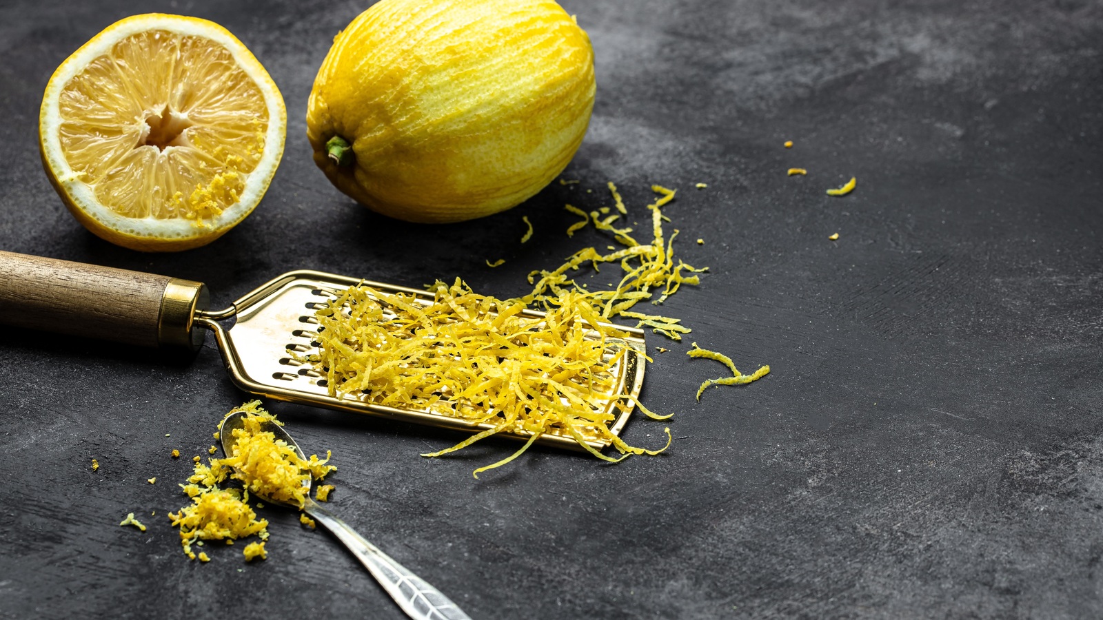 Fresh lemons and grated zest on a grater on a dark surface