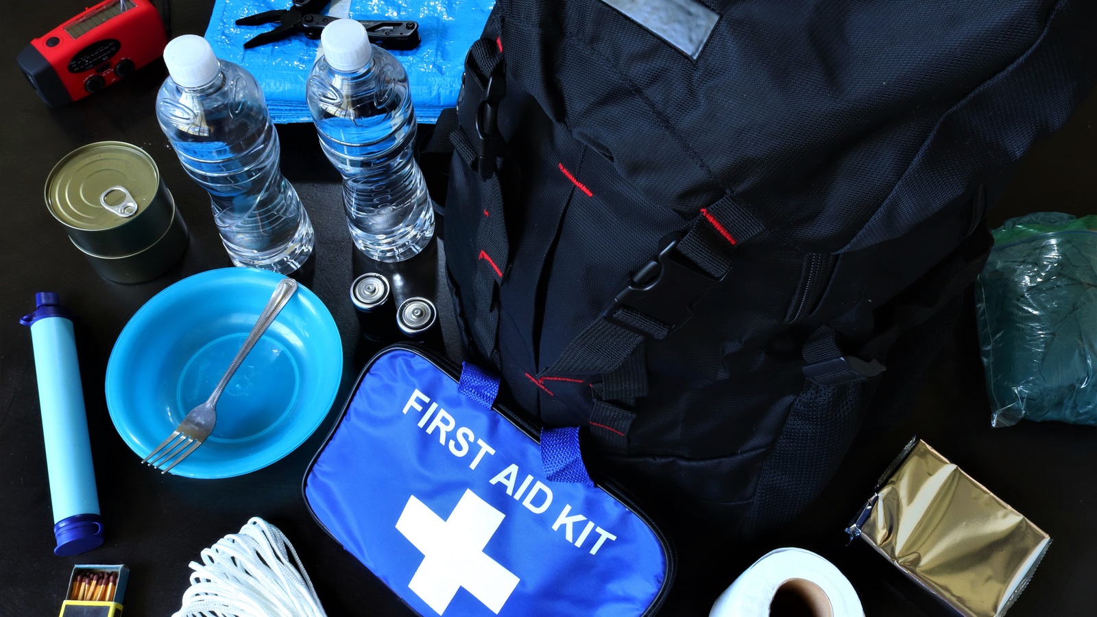 Backpack beside bottled water, flashlight, radio, food and a first-aid kit