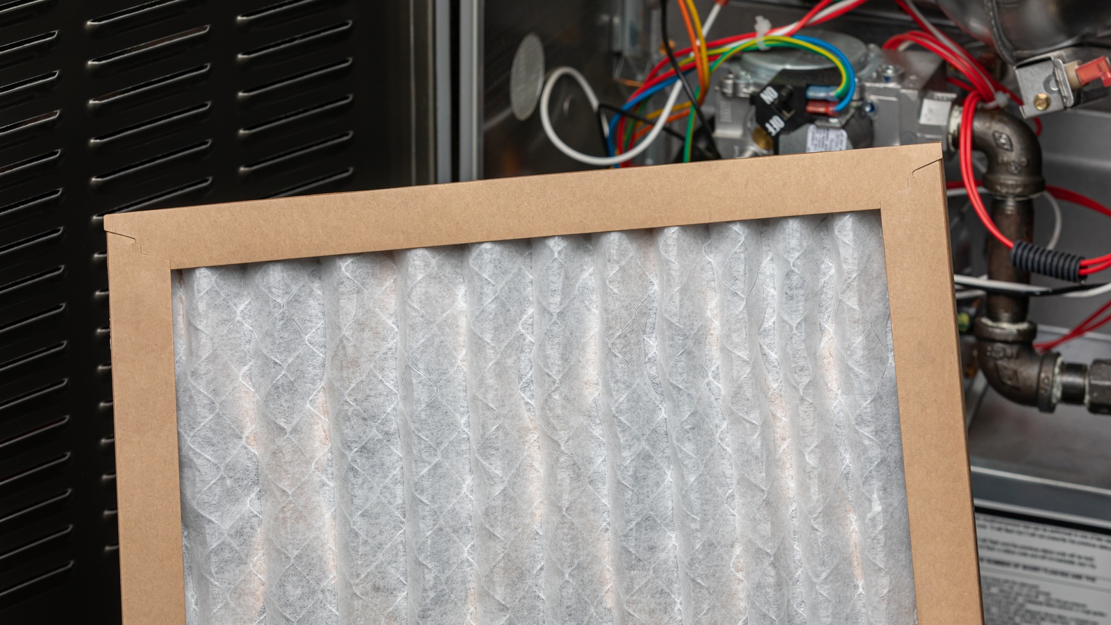 Clean white pleated replacement filter in front of a furnace