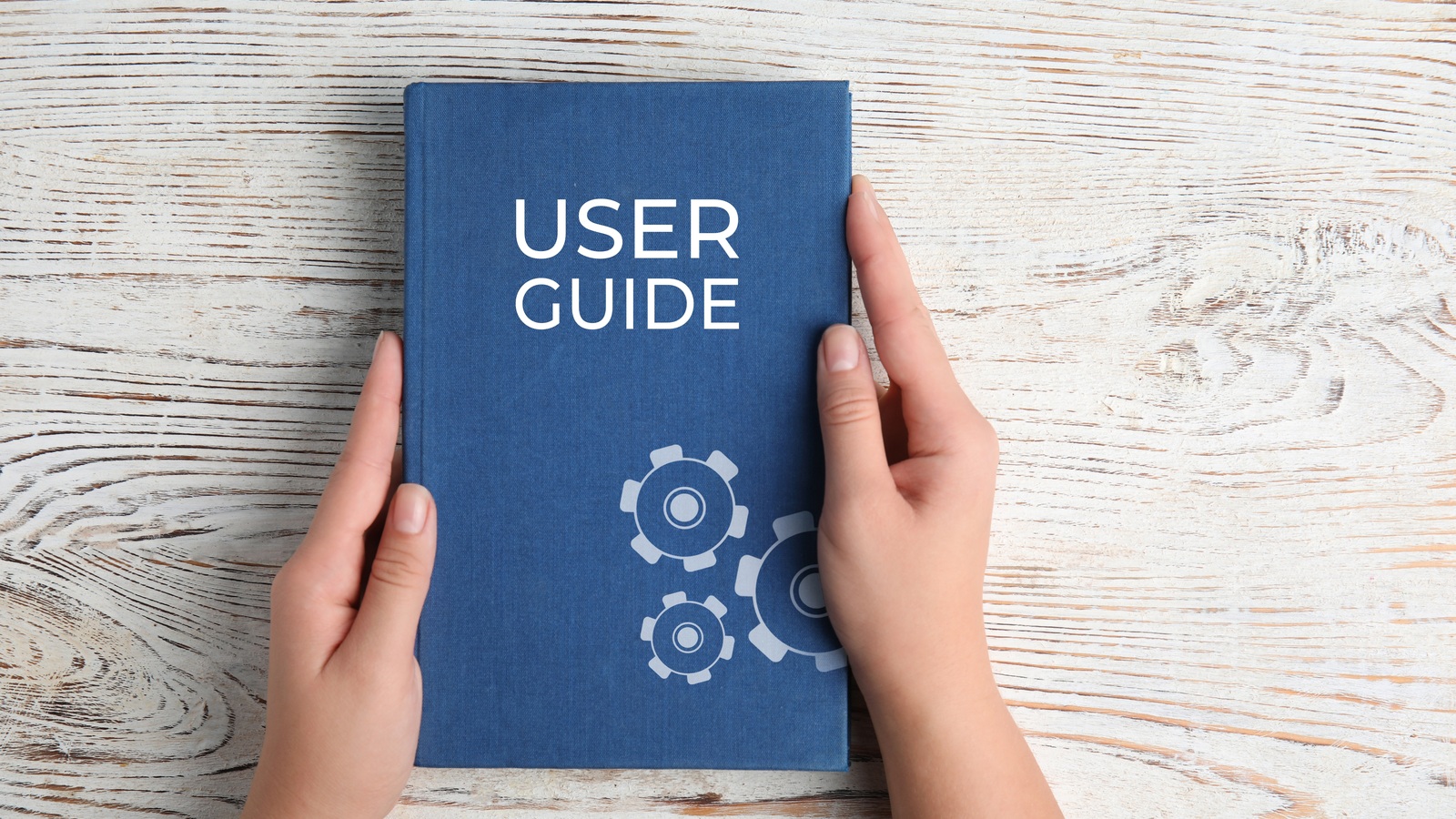 Hands holding a blue user guide booklet on a wooden table