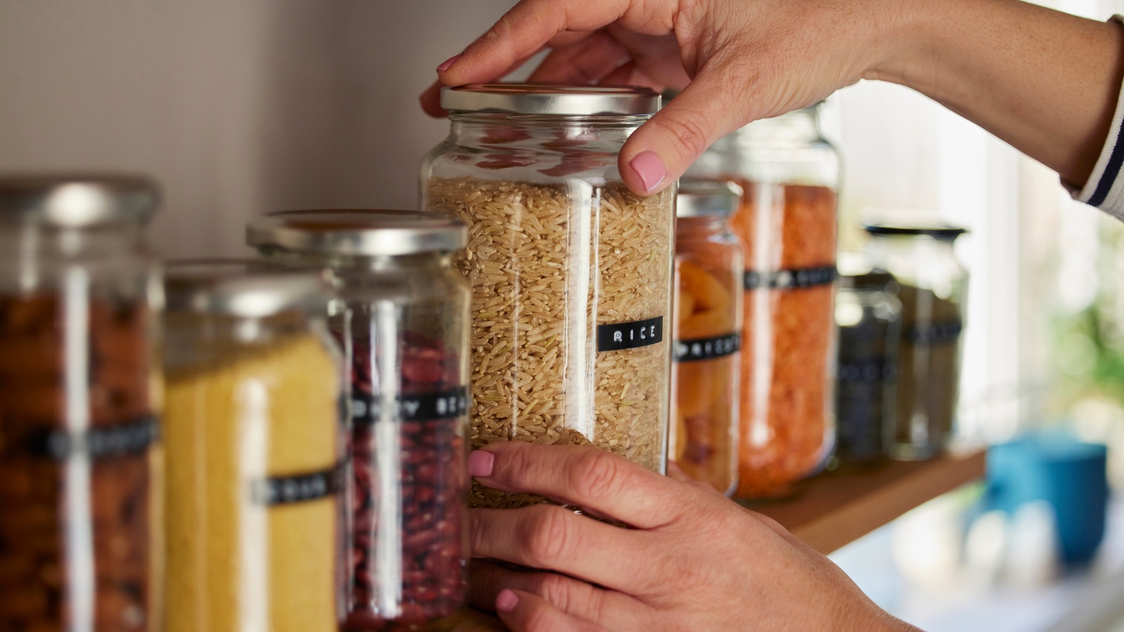 Hands placing a glass jar of rice beside other jars of dried food