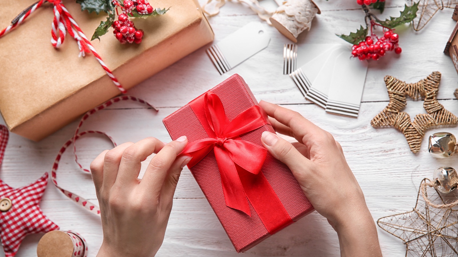 Hands tying a red ribbon around a paper-wrapped gift on a table with twine