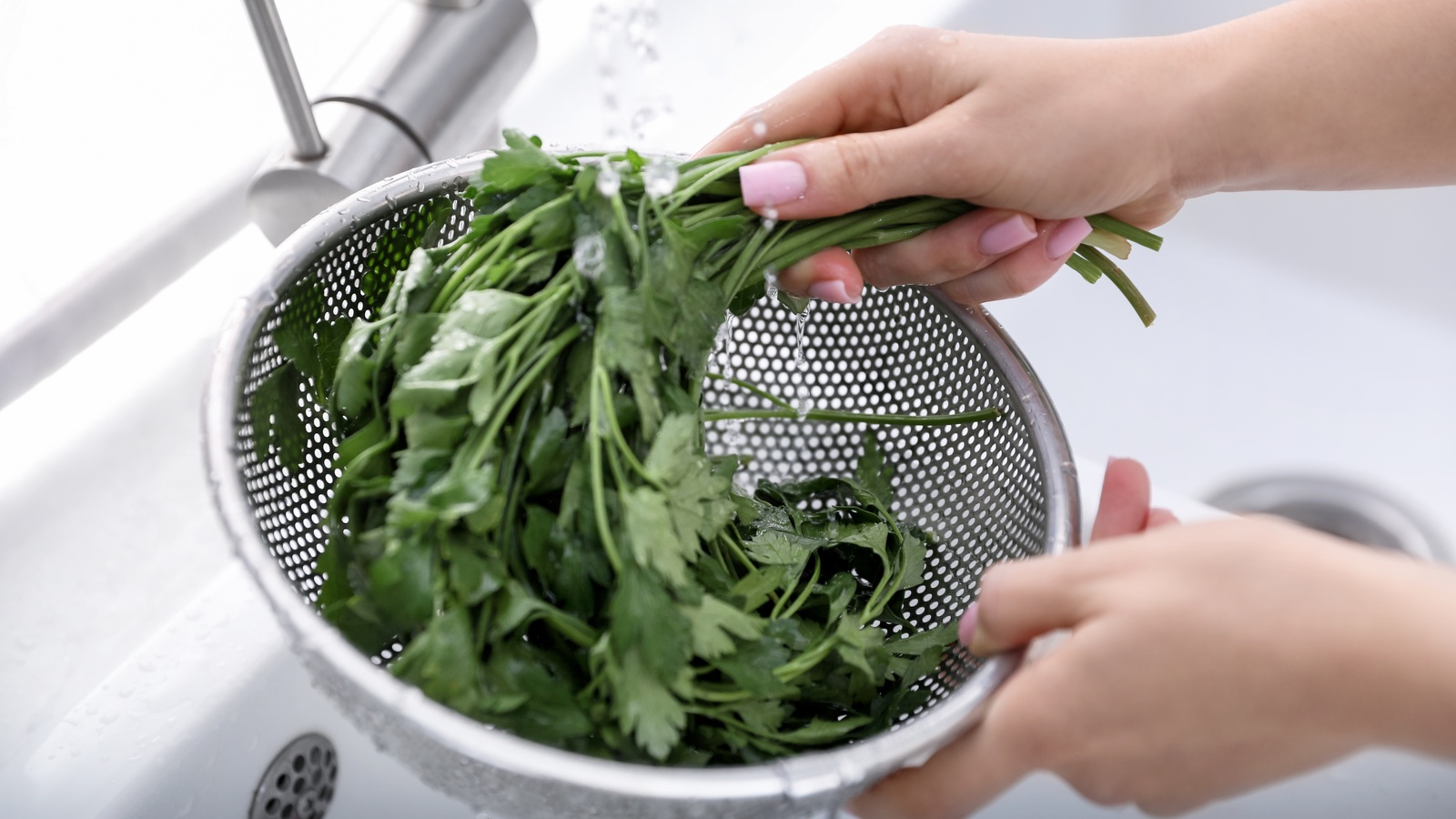 Hands rinsing parsley in a sieve under a running kitchen tap