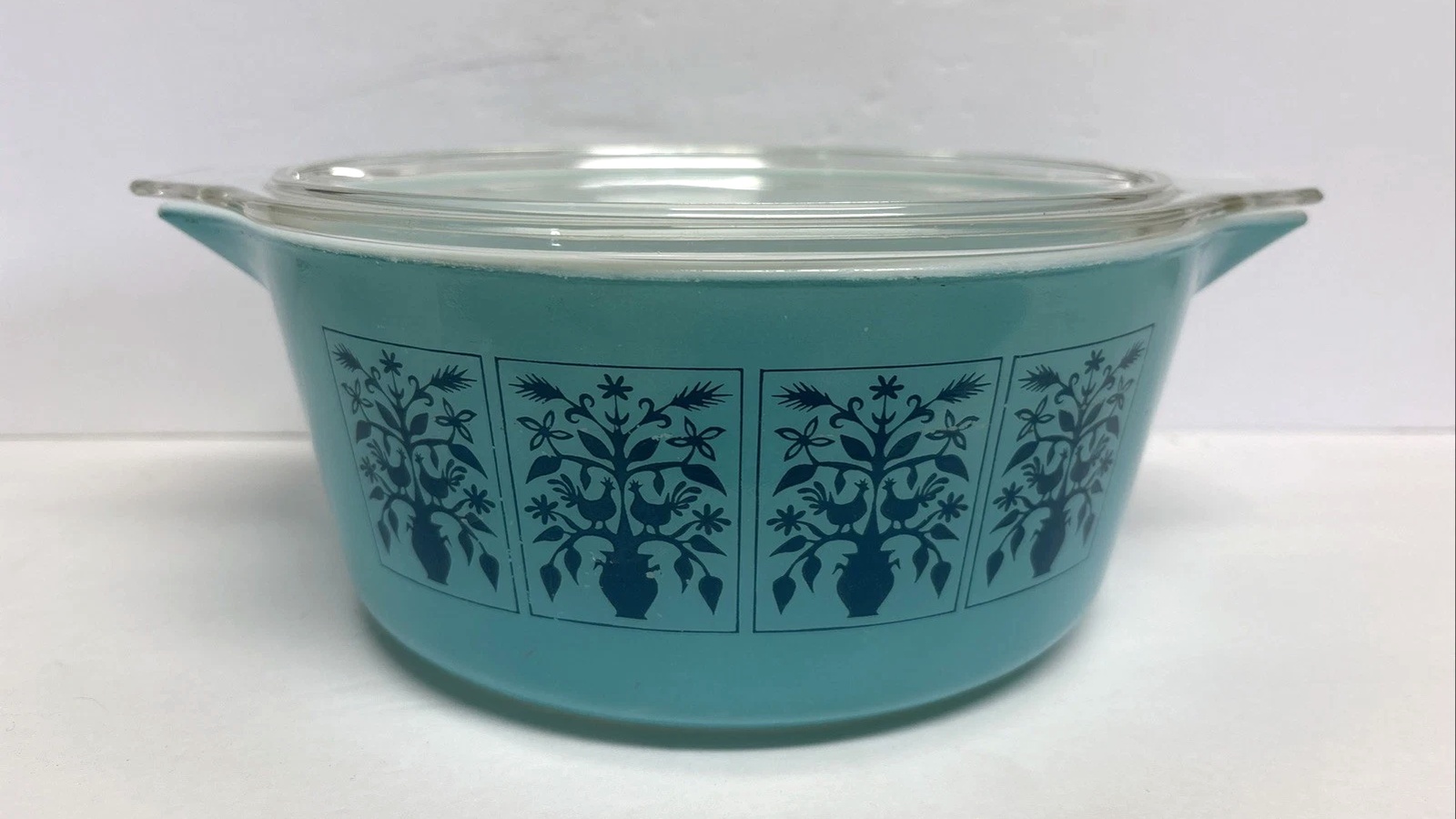 Turquoise Pyrex Saxony casserole with dark blue birds and branches and a clear glass lid