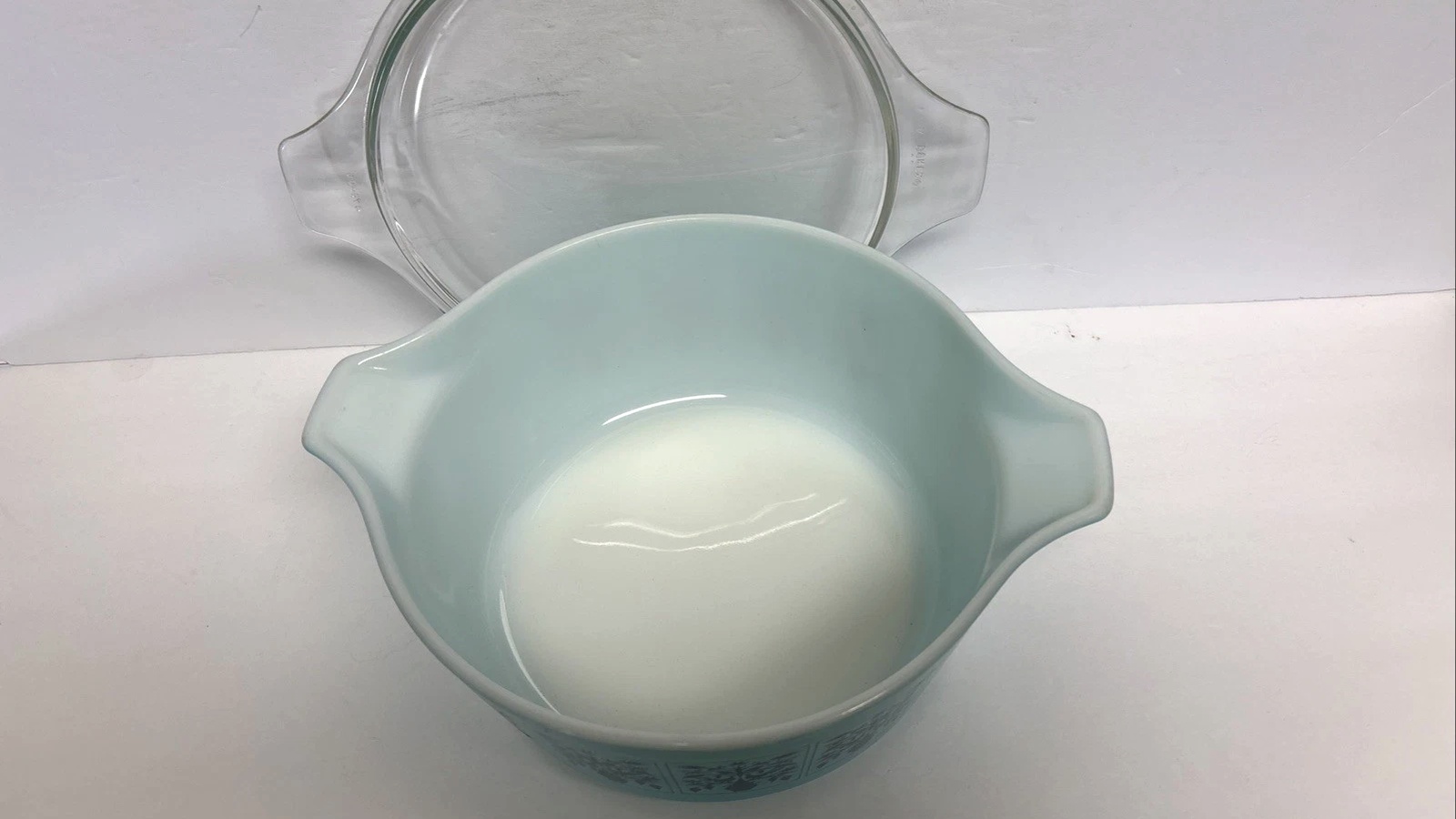 White interior and turquoise rim of an open Saxony Pyrex casserole beside its glass lid