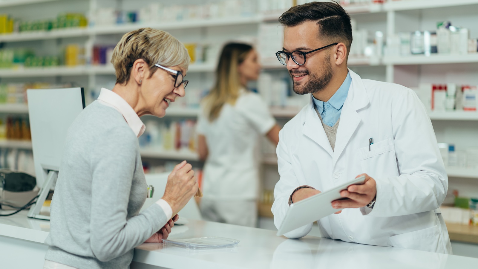 Older customer discussing medication with a pharmacist at a pharmacy counter