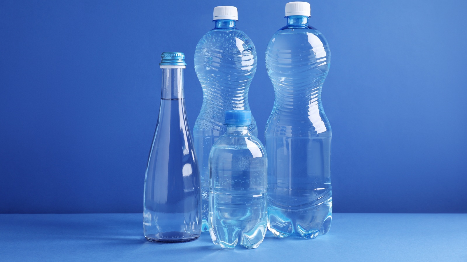 Four capped water bottles in different sizes on a blue tabletop