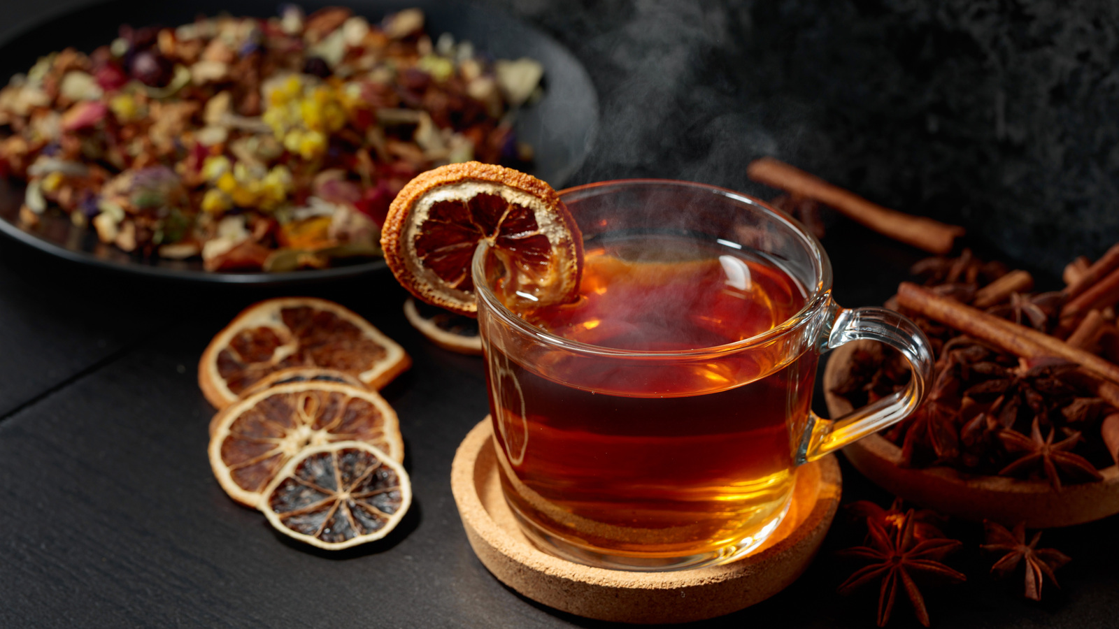 Glass cup of tea with a dried orange slice on the rim and more dried citrus beside it