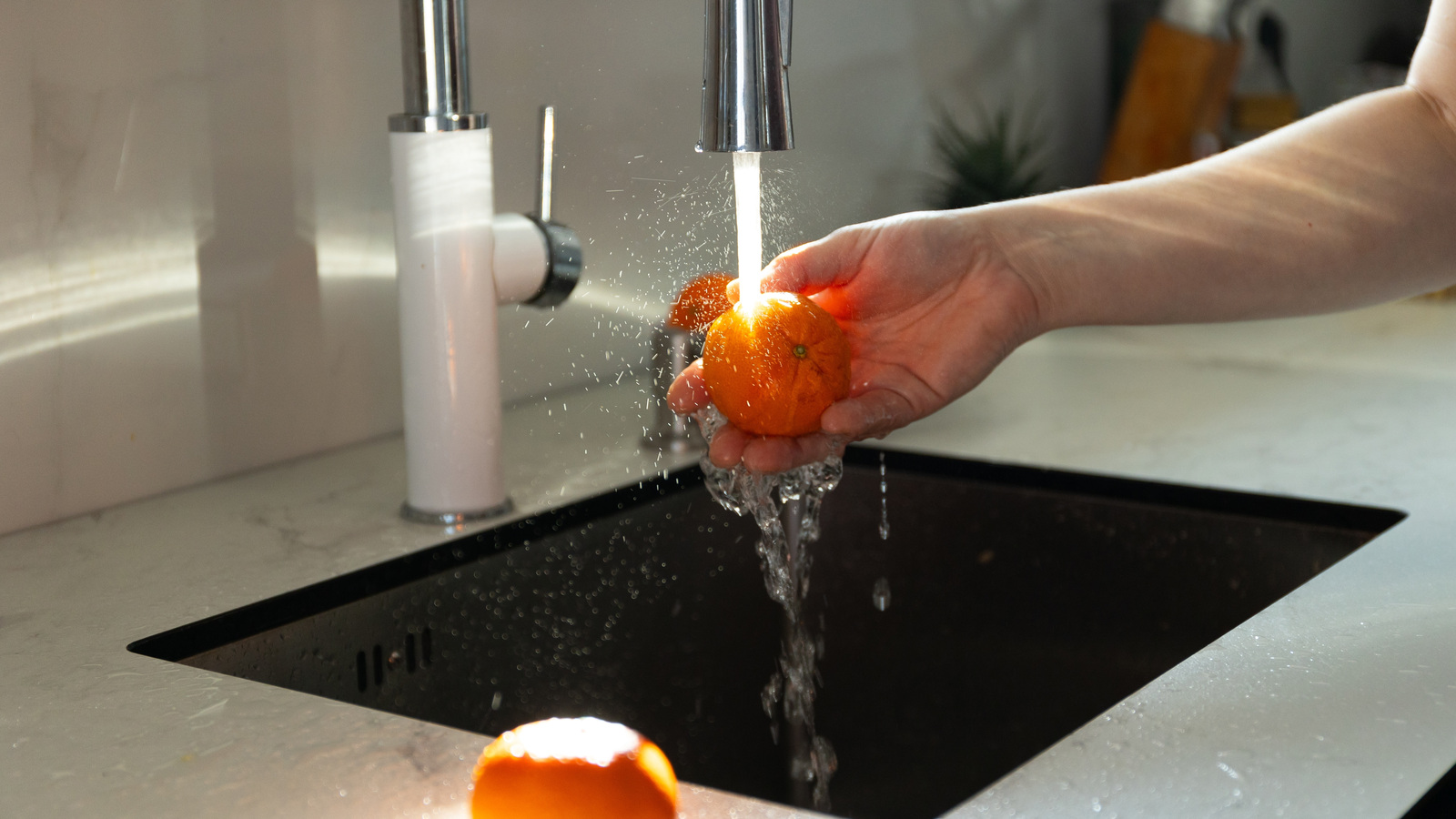 Hand rinsing a whole orange under running tap water