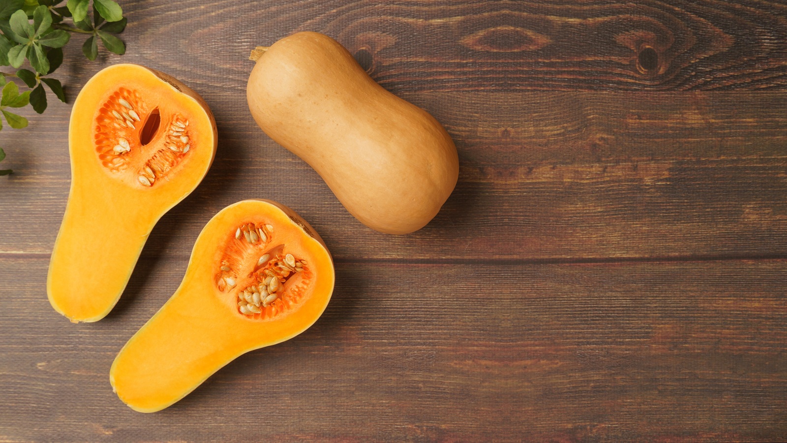 A whole butternut squash with two cut halves showing the seeds