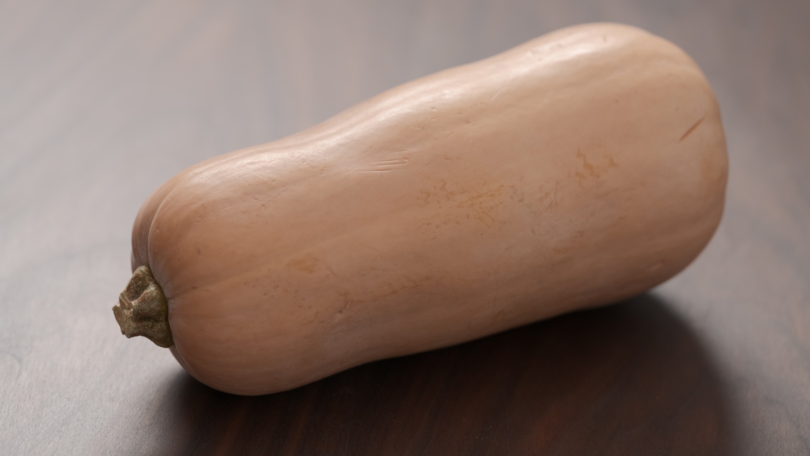 A whole butternut squash with its stalk intact on a wooden surface